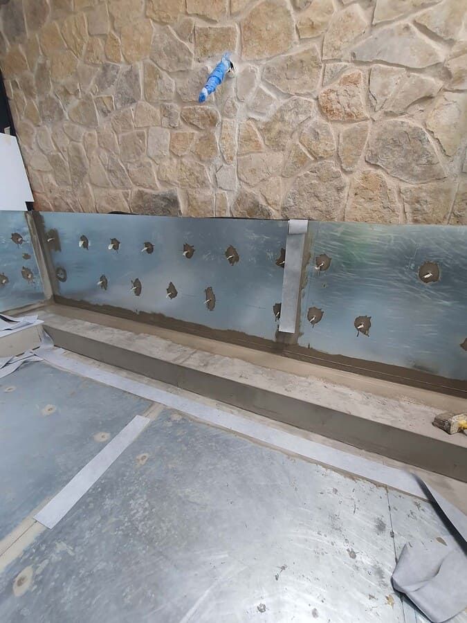 Láminas metálicas fijadas a una pared, posiblemente como parte de un proyecto de construcción. Debajo hay una base de hormigón gris.