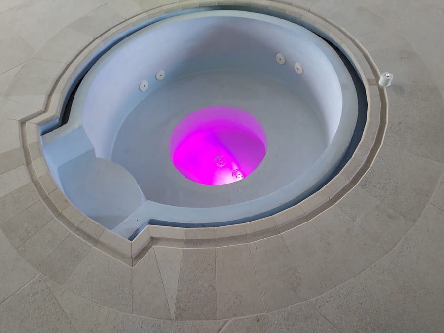 Jacuzzi circular con agua de color violeta brillante rodeada de baldosas de piedra.
