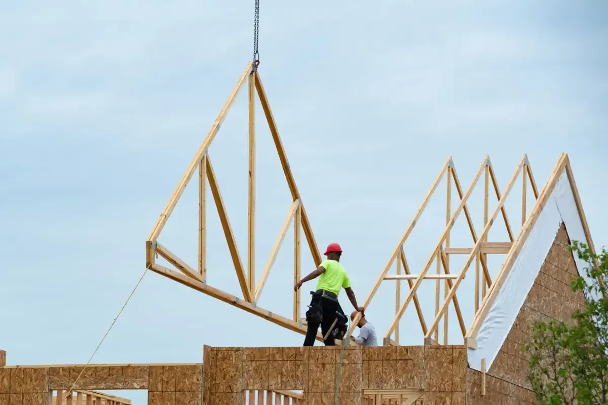 Obreros de la construcción instalando una armadura de techo de madera en un edificio nuevo bajo un cielo nublado.