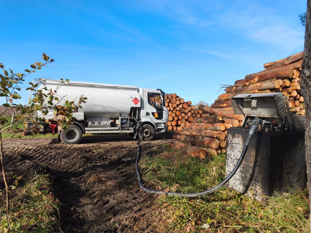 Camion-citerne à carburant, relié à un distributeur dans une zone boisée par temps clair.