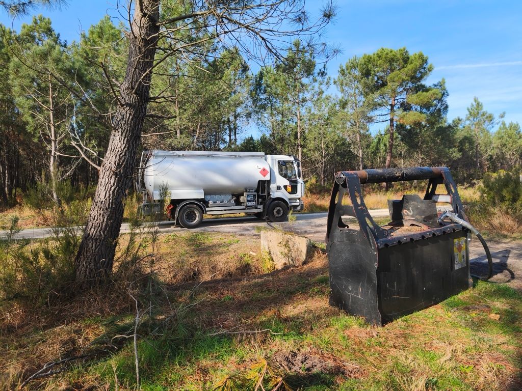 Camion-citerne sur une route dans une zone boisée, avec une citerne au premier plan.