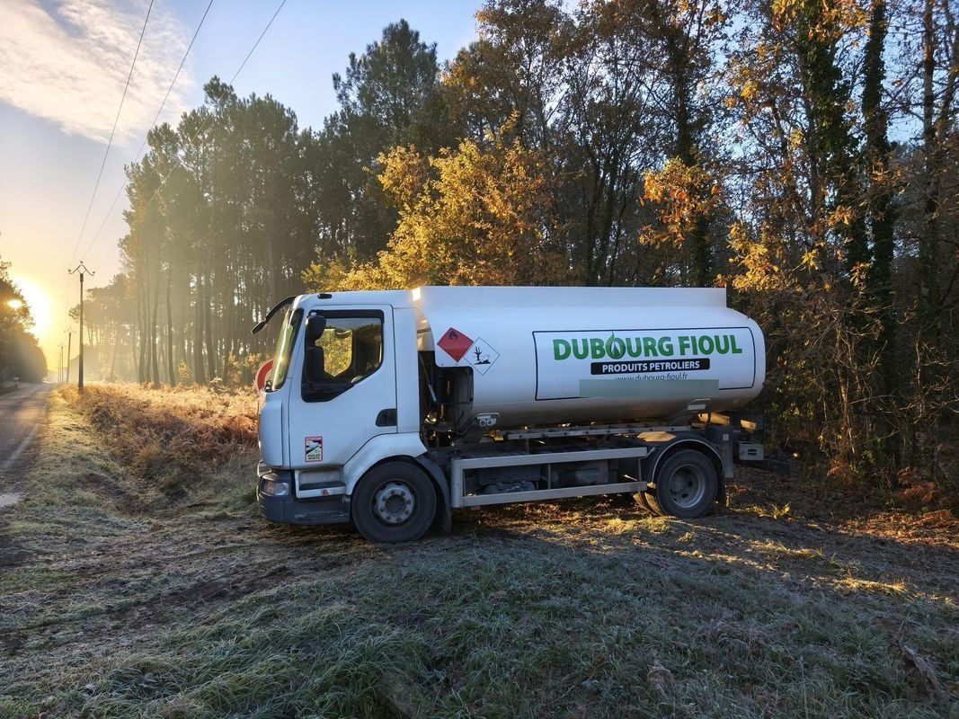 Camion-citerne blanc de la société DUBOURG FIOUL sur un chemin de terre dans une zone boisée.