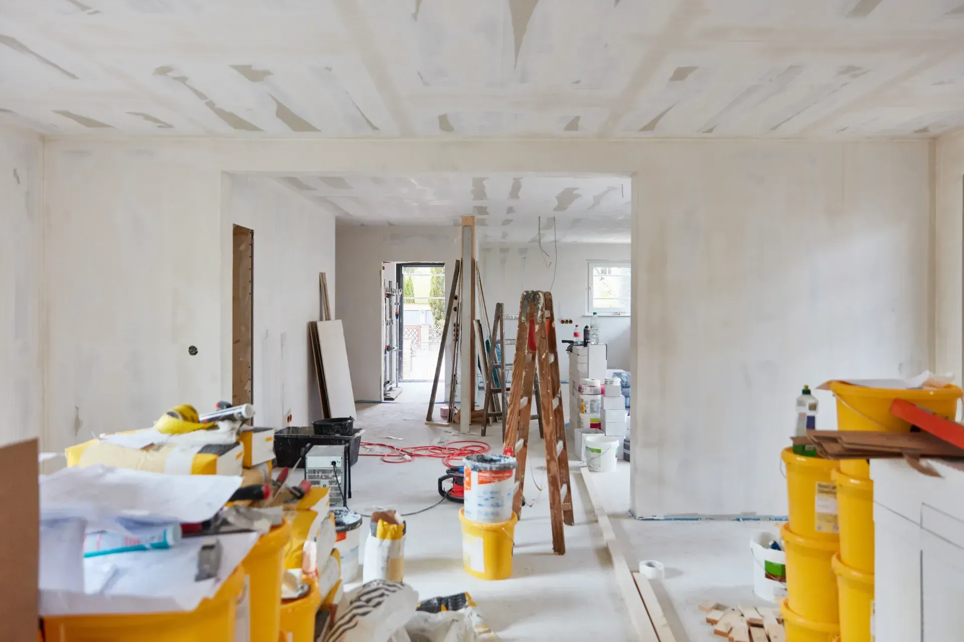 Una habitación en construcción con una escalera y baldes de pintura.
