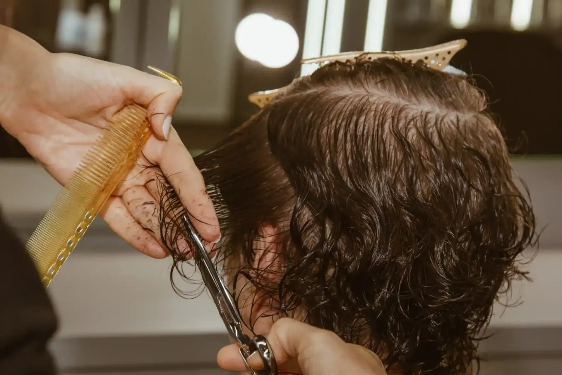 En un salón de belleza, un estilista utiliza tijeras y un peine para recortar el cabello húmedo y rizado de una persona.