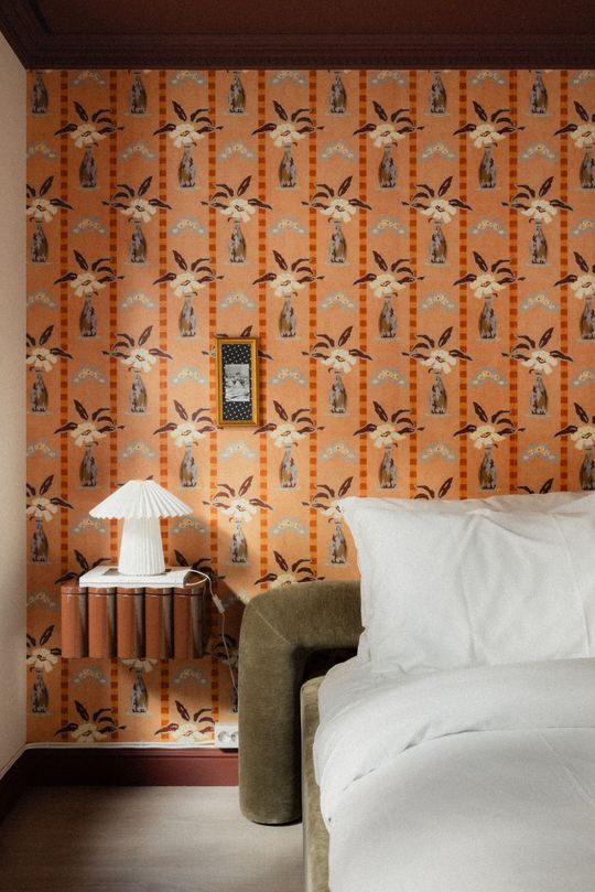 Cozy bedroom with orange patterned wallpaper, white bed, and a small table lamp beside the bed