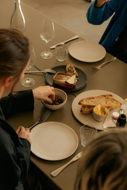 People serving food at a dining table with plates, bread, and wine glasses