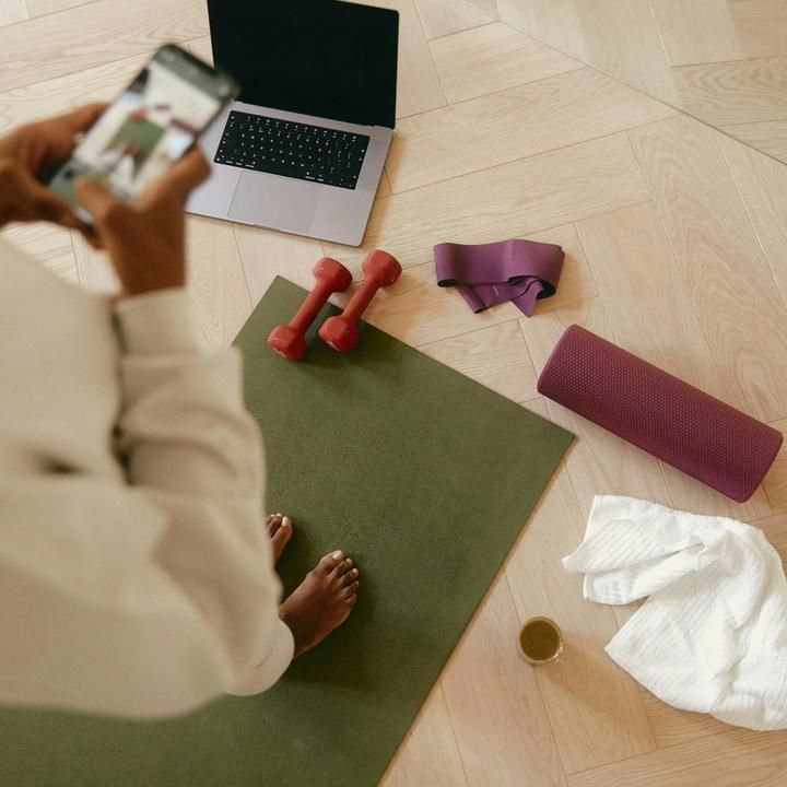 Guest with a phone on a yoga mat, with dumbbells, a laptop and a foam roller on the floor