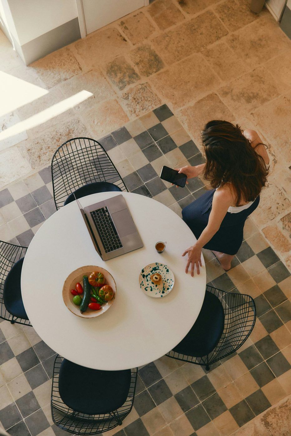 Guest with a phone by a table with a laptop, coffee and breakfast, seen from above