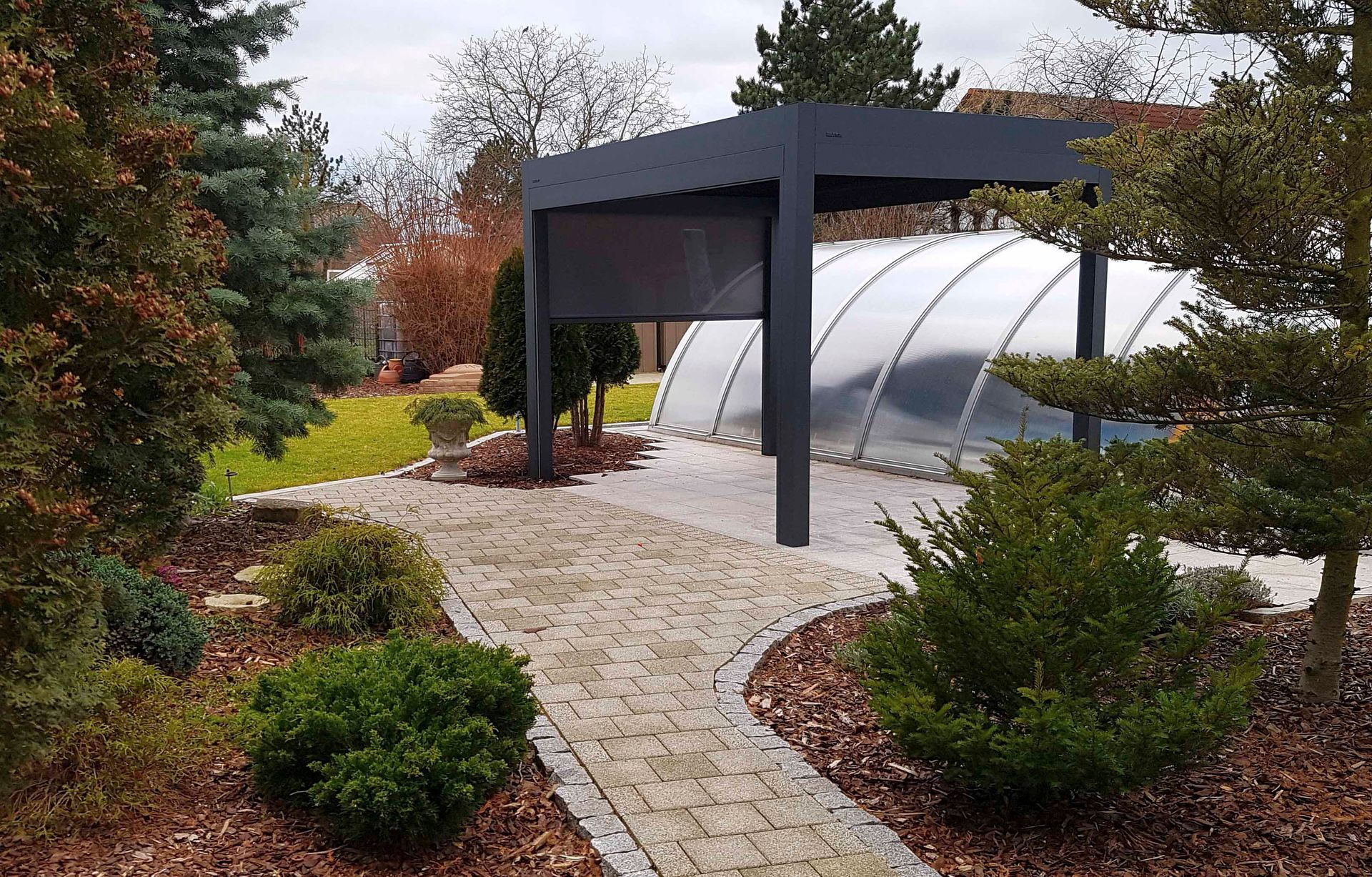 Weg führt zum Pool mit schwarzer Pergola, umgeben von Grün und Garten.