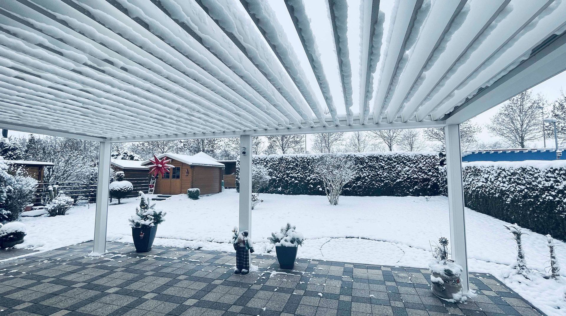 Schneebedeckte Terrasse mit Pergola, Garten und verschneitem Hinterhof.