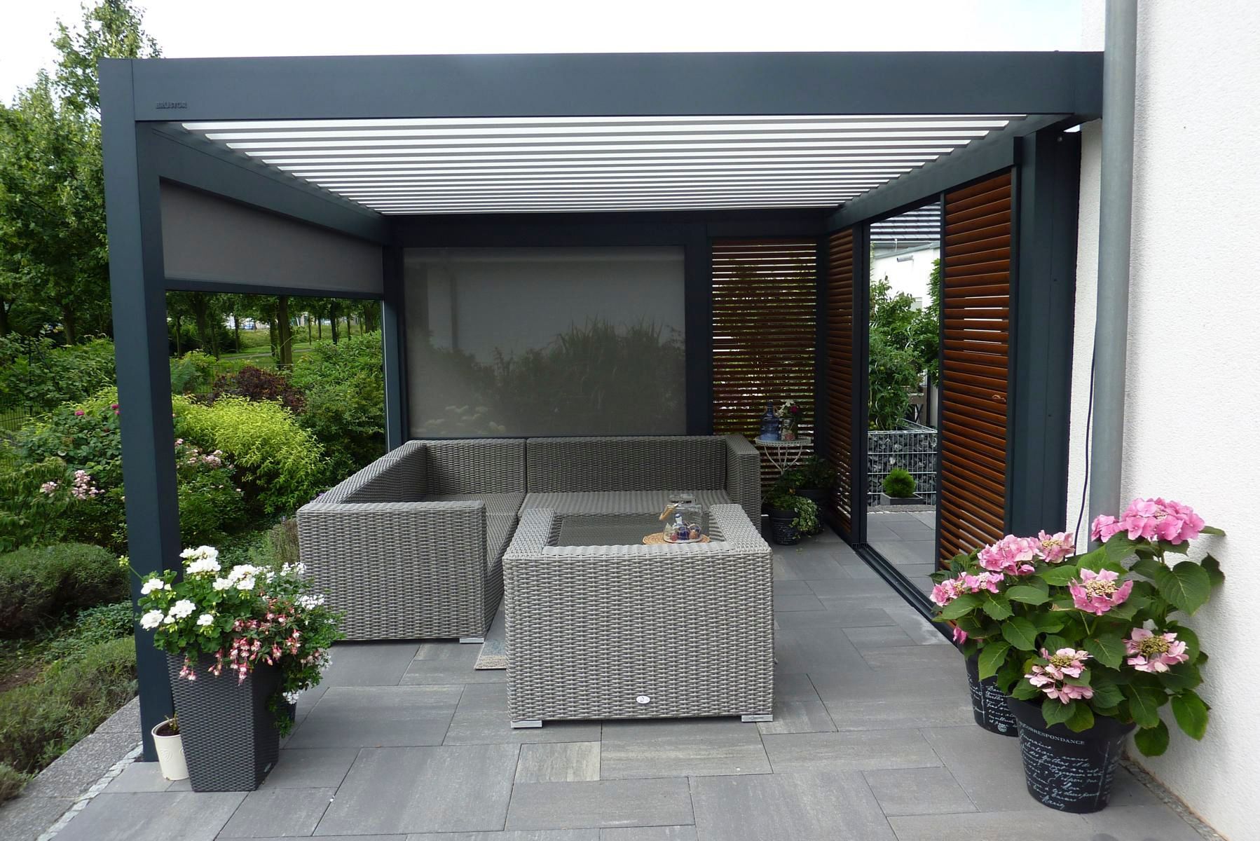 Außenterrasse mit grauen Korbmöbeln, Pergola und Topfblumen.