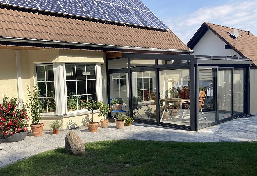 Wintergartenanbau an einem Haus mit Solarmodulen, Topfpflanzen und einer Steinterrasse.