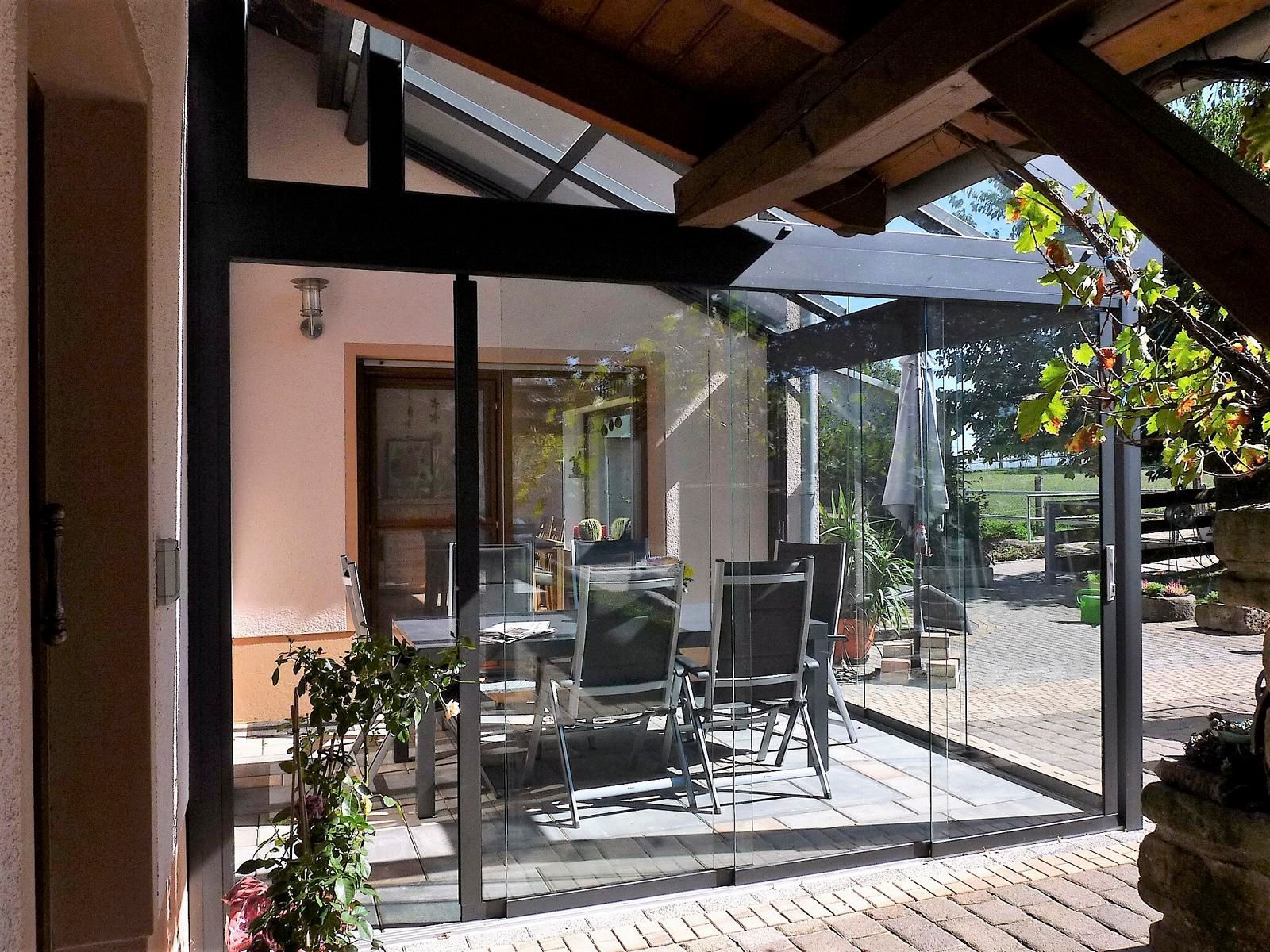 Terrasse mit Glaswänden, Tisch und Stühlen; Blick von einer überdachten Veranda.