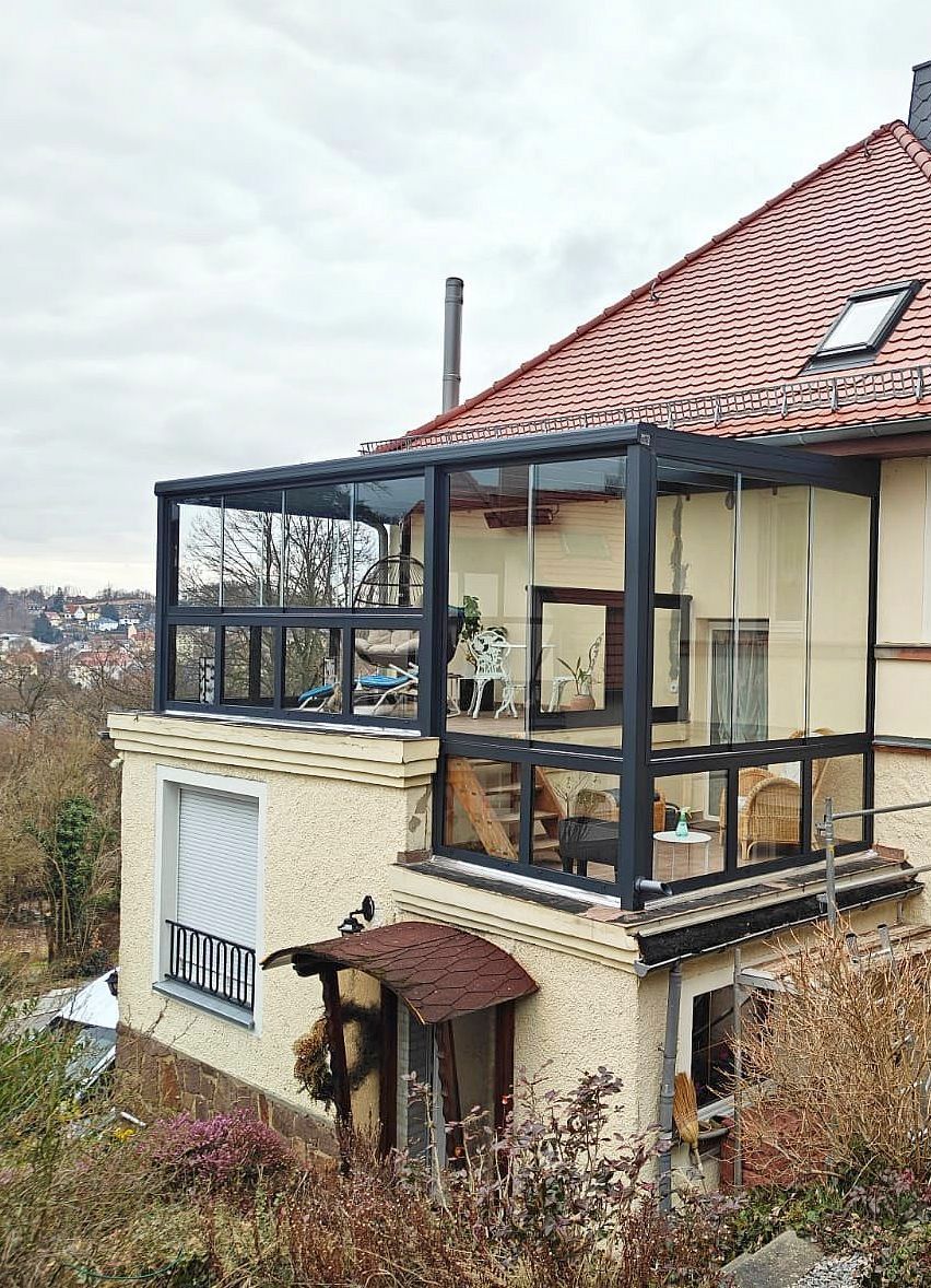 Zweistöckiges Haus mit Balkonanbau mit Glaswänden und Blick auf die Stadtlandschaft. Bewölkter Tag.