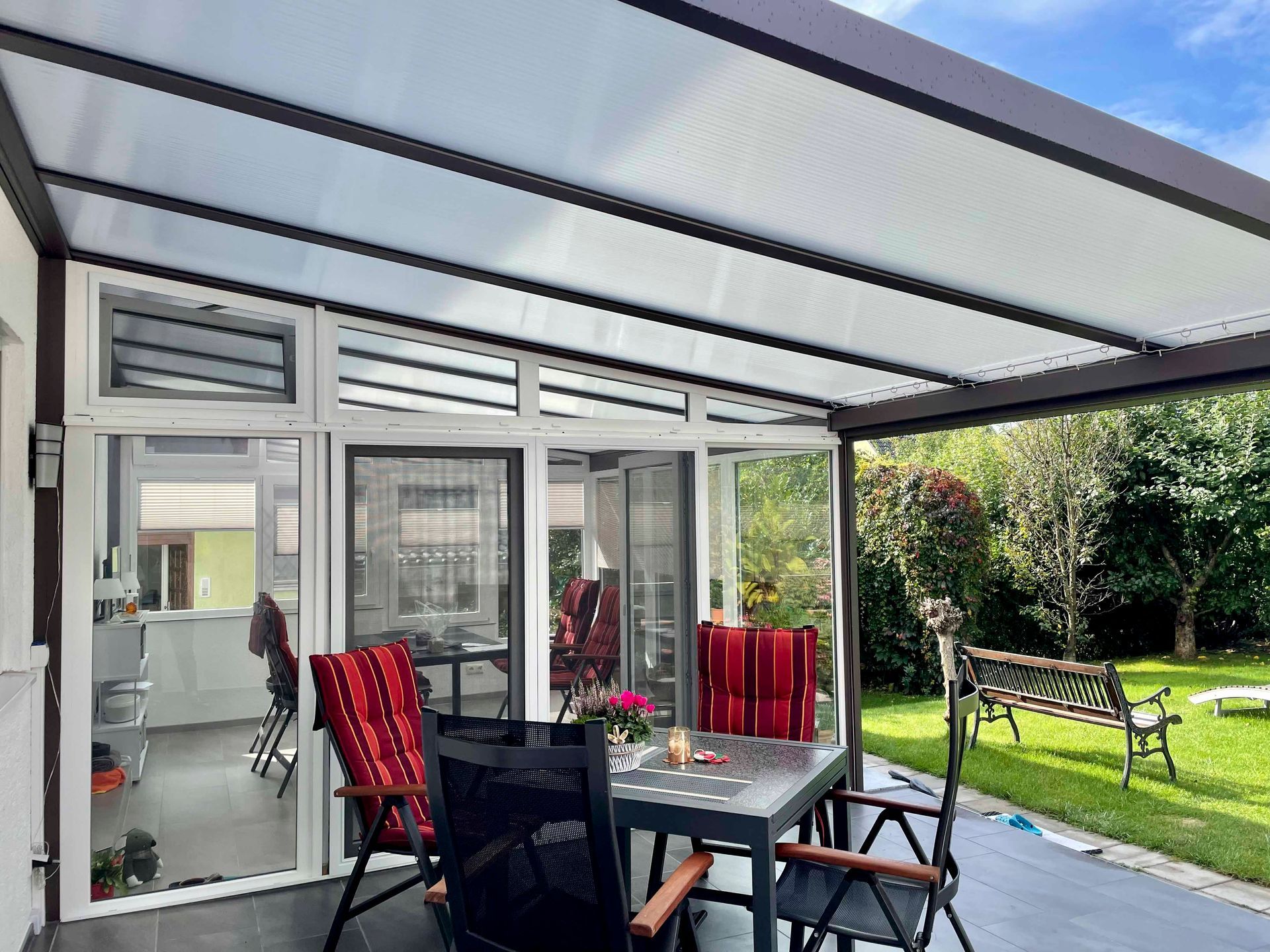 Terrasse mit durchsichtigem Dach, Tisch, Stühlen und Blick auf den Garten.