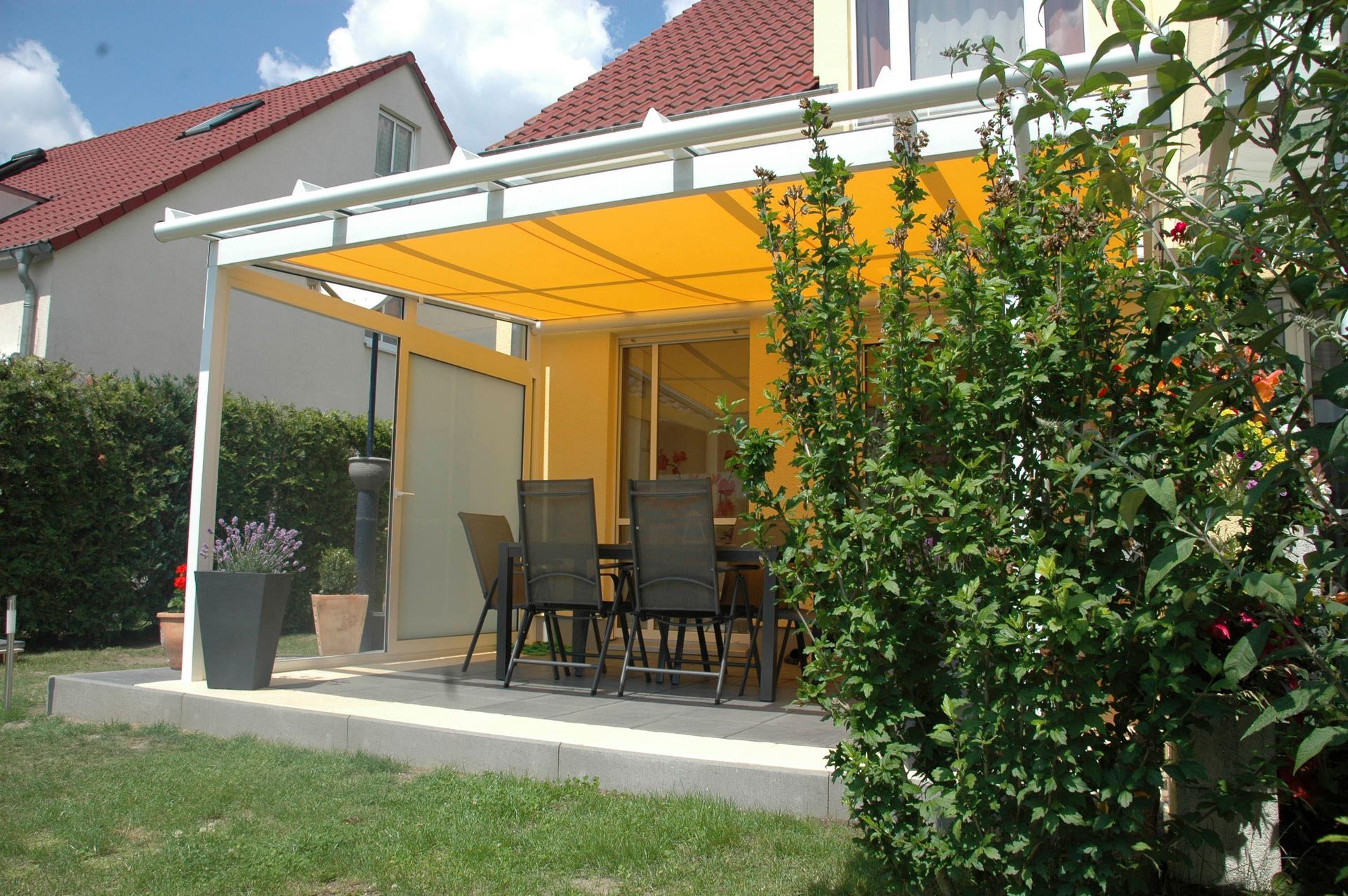 Gelbe Terrassenmarkise über einem Essbereich im Freien; sonniger Hinterhof.