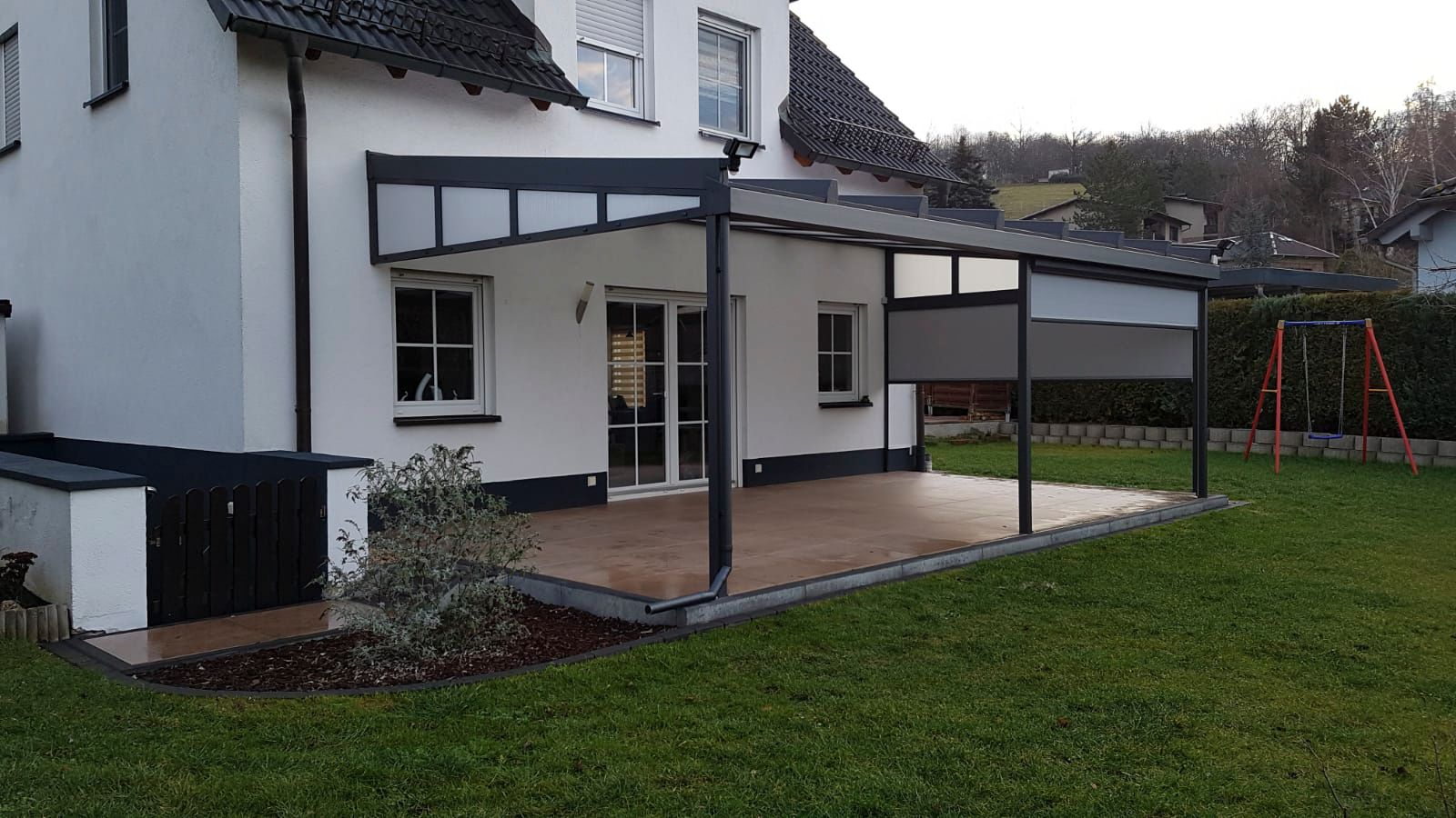 An einem weißen Haus mit Glastüren angebrachte Pergola mit Blick auf einen grünen Rasen.