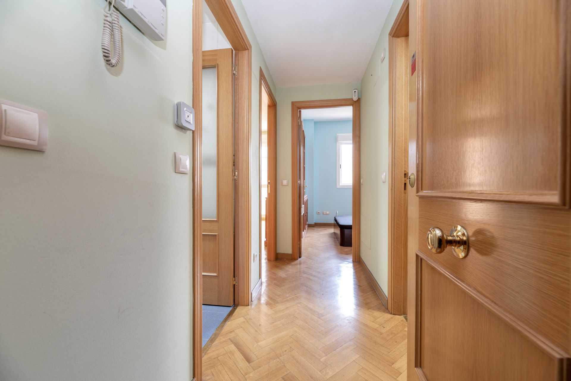 Couloir étroit au sol en bois, avec des portes ouvertes et de la lumière du jour au fond.