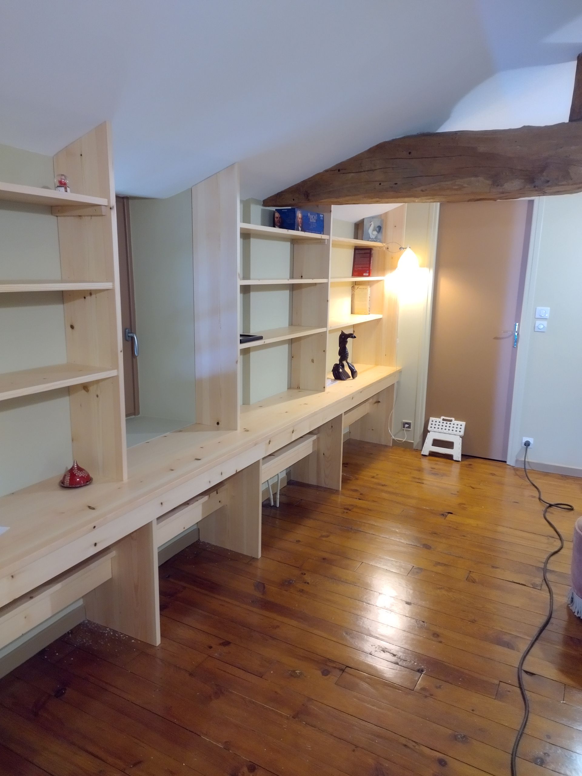 Étagères et bureaux intégrés dans une pièce mansardée lumineuse, avec parquet et poutres apparentes