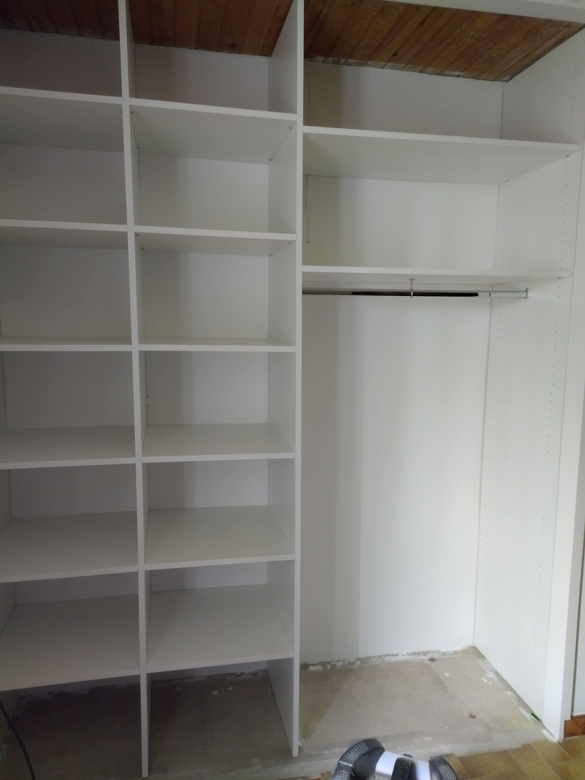 Placard blanc vide avec des étagères intégrées et un espace de penderie sous un plafond en bois.