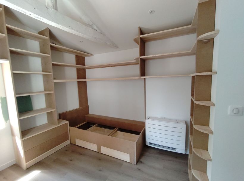 Étagères d’angle et tiroirs intégrés dans une petite pièce blanche faisant office de dressing