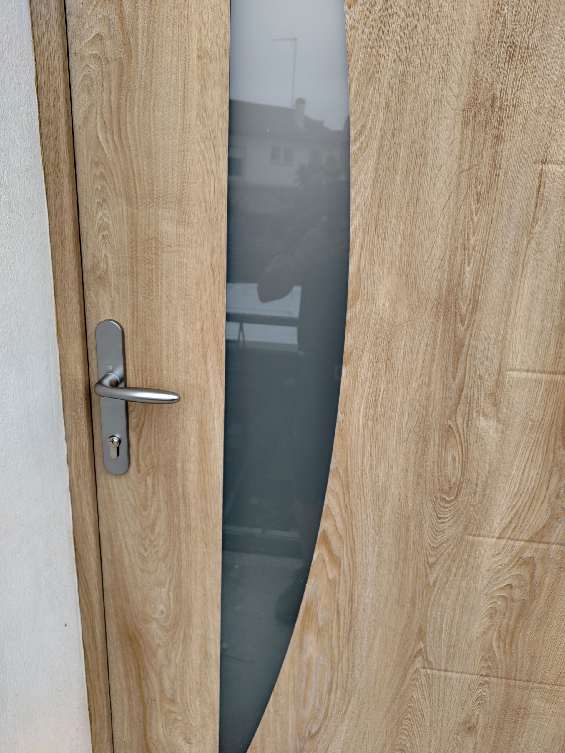Porte en bois entrouverte, avec une poignée argentée et un panneau en verre dépoli