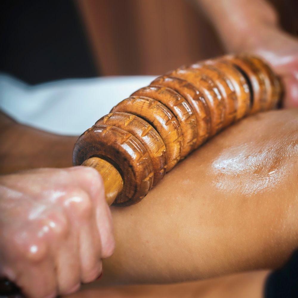 Primer plano de la pierna de una persona recibiendo un masaje con un rodillo de madera. La pierna está aceitada.