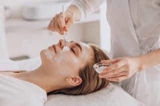 Una esteticista aplica un sérum facial a una clienta recostada en una camilla de spa