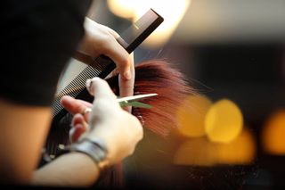 Manos cortando el cabello castaño rojizo con unas tijeras y un peine, en primer plano en un salón