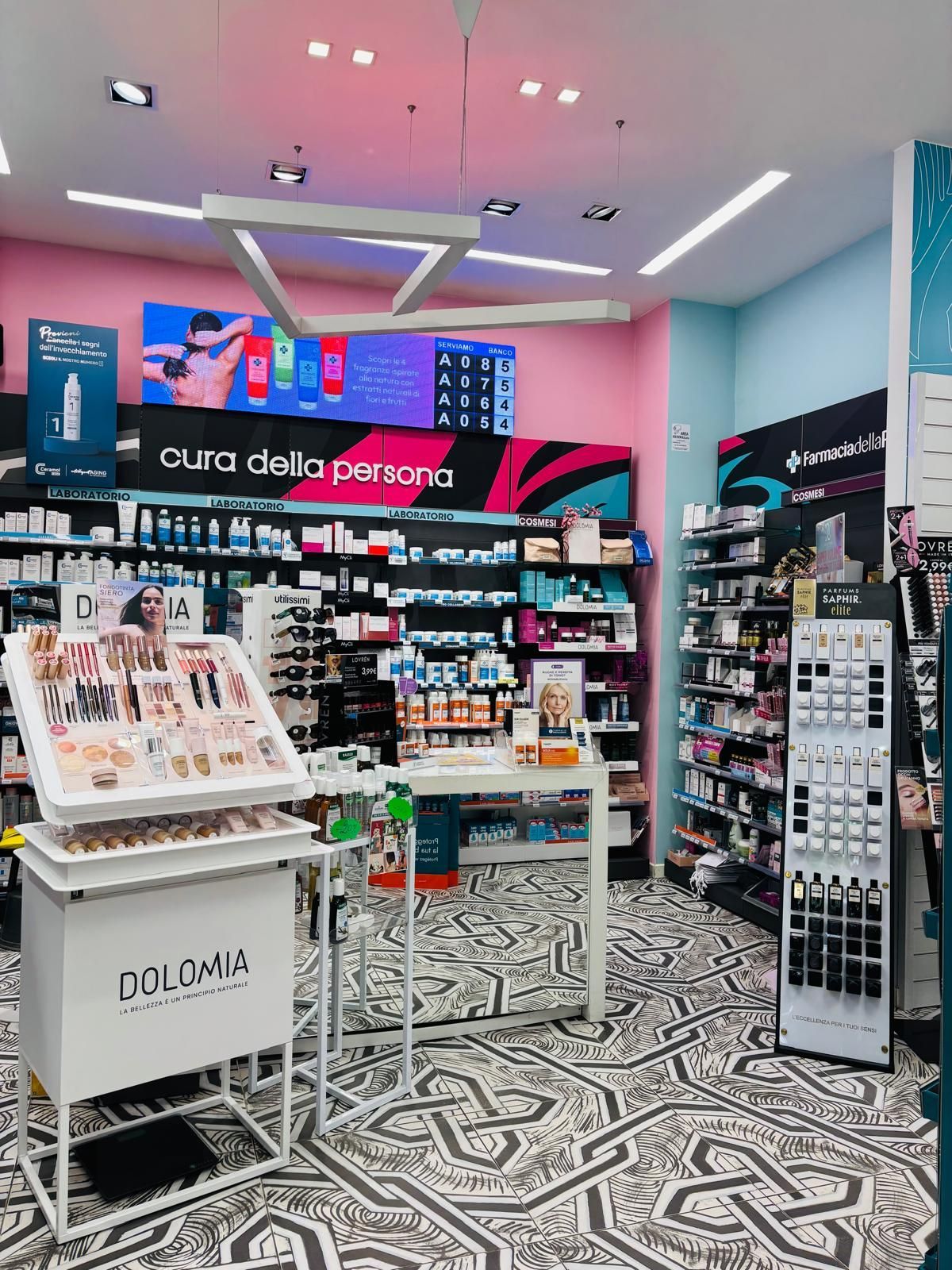 Corridoio luminoso, cosmetici con scaffali espositivi, pareti rosa e piastrelle del pavimento decorate.