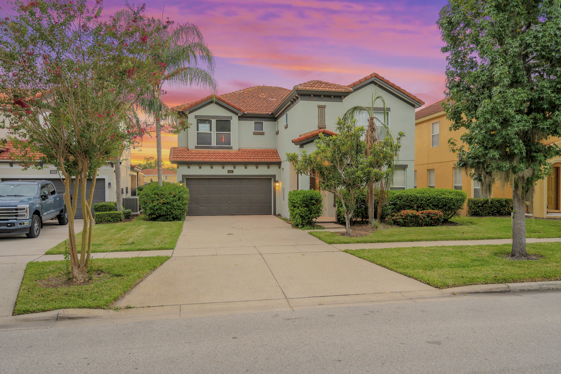 Two-story vacation home with a driveway and lawn under a colorful Orlando sunset sky.