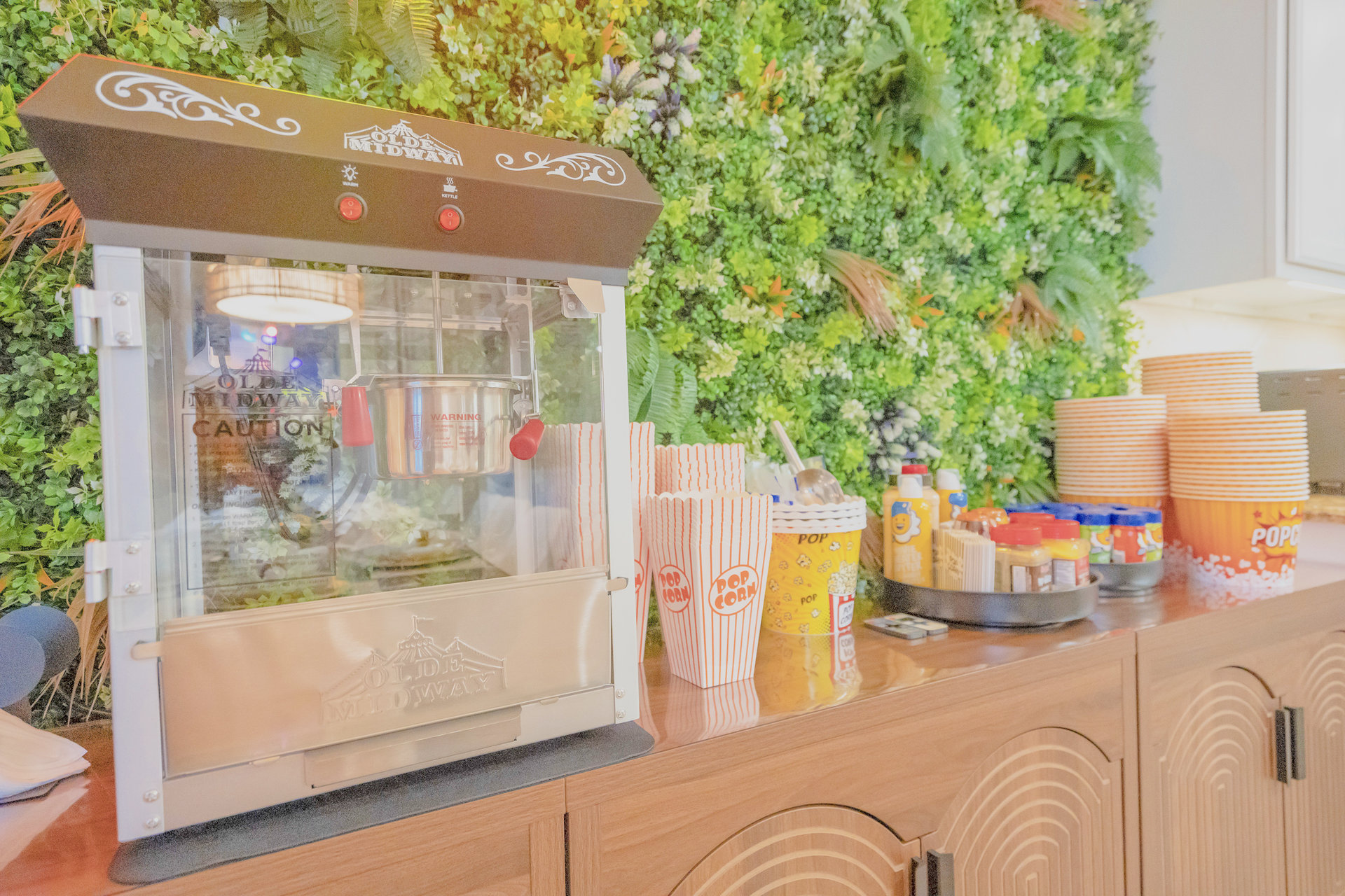 Popcorn machine on a wooden counter with snacks and green wall backdrop.
