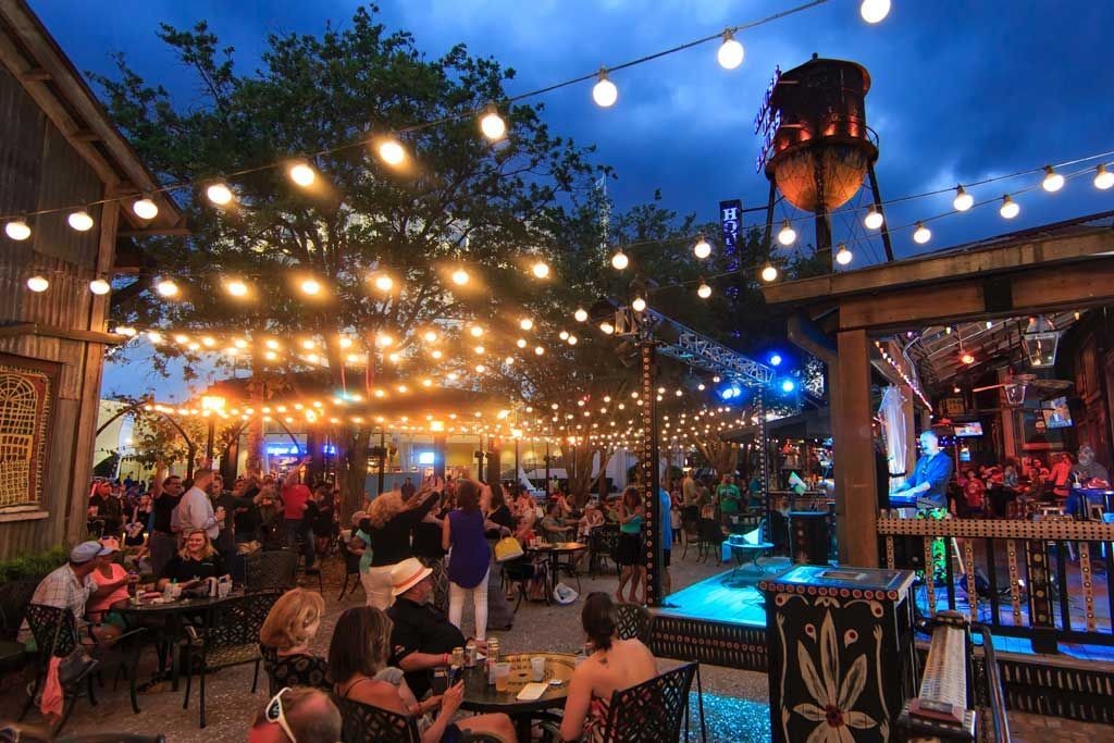 An outdoor evening scene at a restaurant with string lights, a water tower, and a live band.