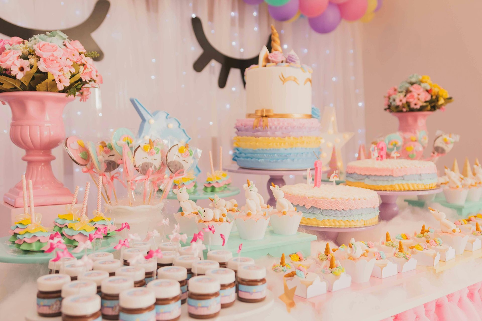 Unicorn-themed dessert table with cake, cupcakes, and candy in pastel colors; flowers and decorations.