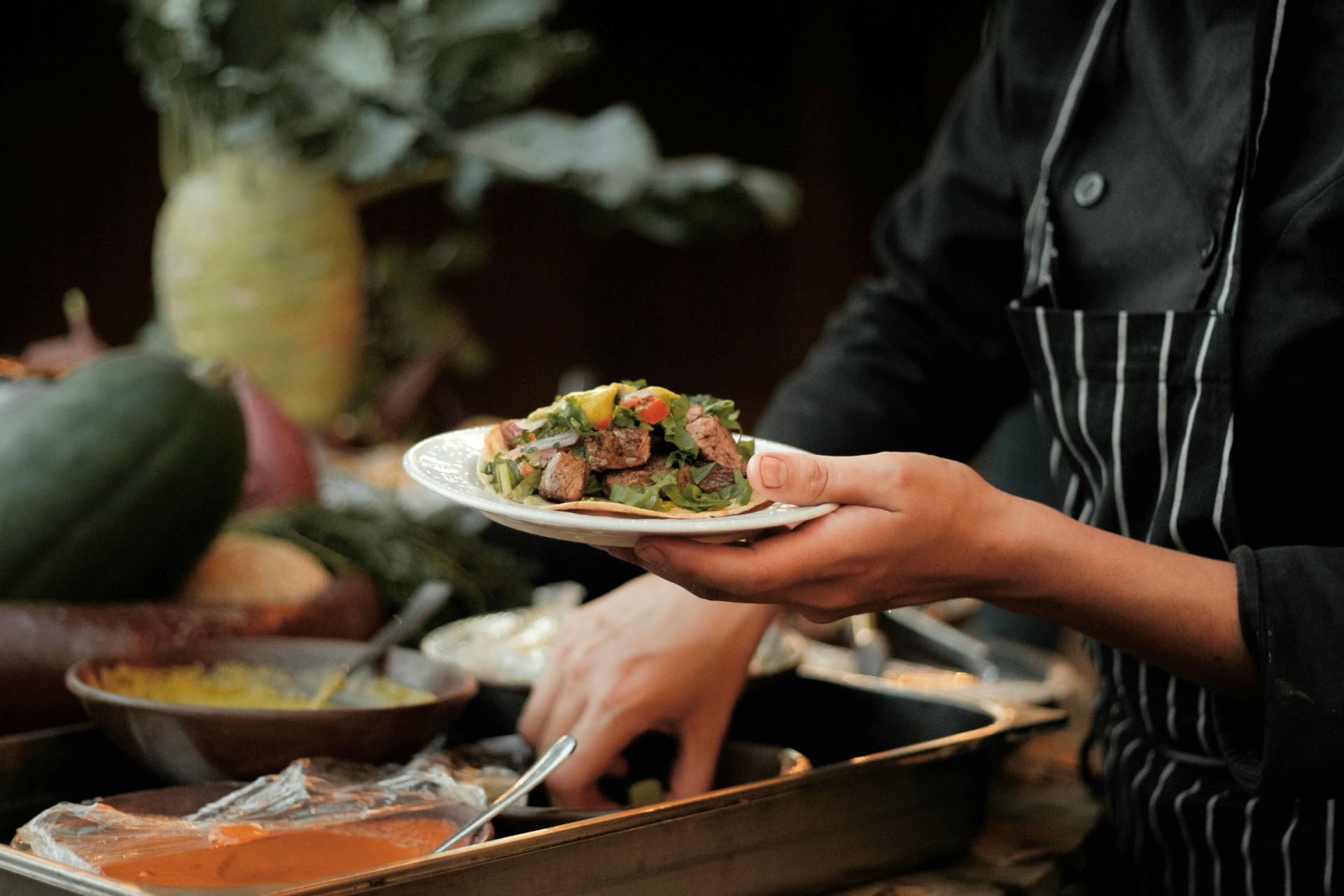 Chef holding a plate of salad with hands near a food prep station.