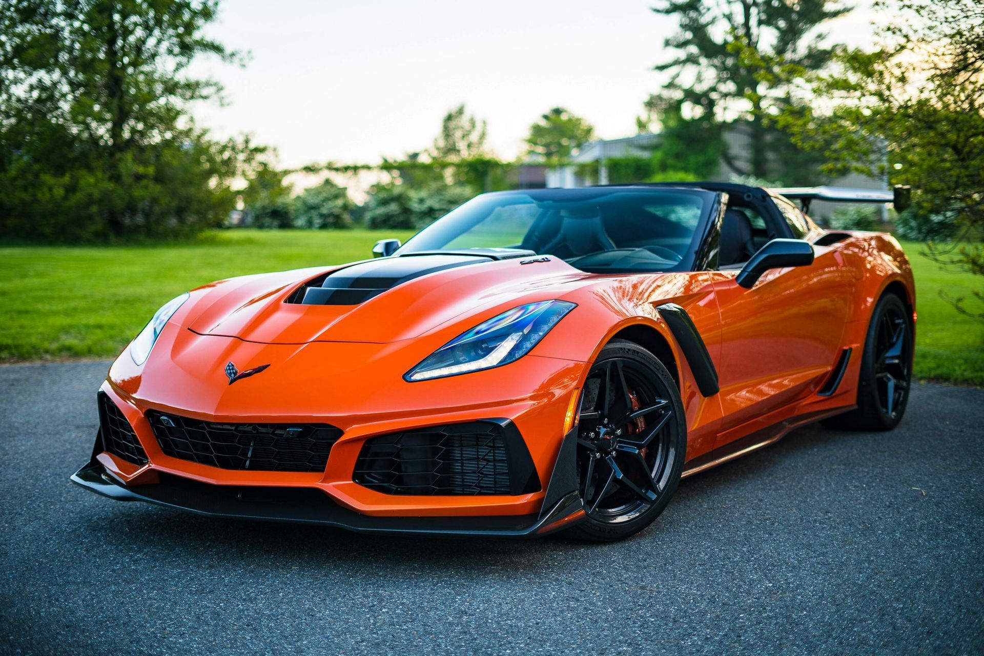 Orange sports car parked on a driveway; black accents, sunny outdoors.
