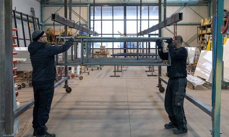 Zwei Männer arbeiten an einer Metallkonstruktion in einer Fabrik.