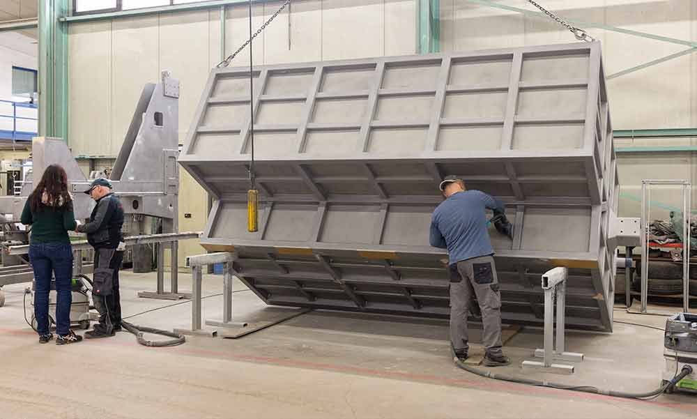 Zwei Männer arbeiten in einer Fabrik an einem großen Stück Metall.