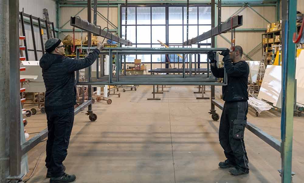 Zwei Männer arbeiten an einer Metallkonstruktion in einer Fabrik.