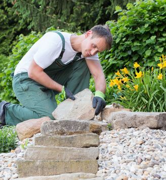 Ein Mann kniet nieder, um einen Stein in einem Garten aufzuheben
