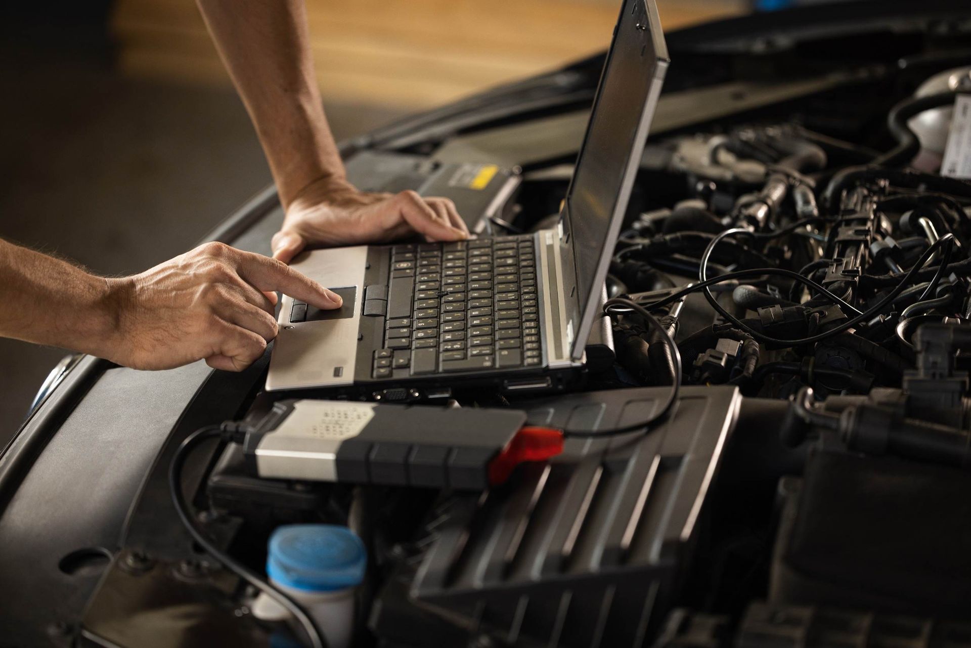 Una persona está usando una computadora portátil debajo del capó de un automóvil.