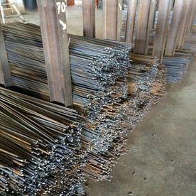 Montones de varillas metálicas apiladas en un taller, con los extremos cortados visibles sobre un suelo de hormigón.