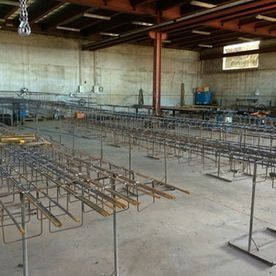 Almacén interior con filas de armazones de barras de refuerzo metálicas sobre un piso de concreto y vigas expuestas en el techo.
