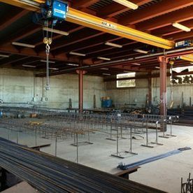 Interior de la obra en construcción con barras de acero de refuerzo, losa de hormigón y vigas de grúa aérea.