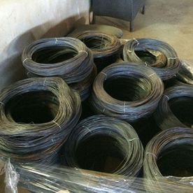 Bobinas de alambre oscuro apiladas en el suelo en un espacio que parece un almacén.