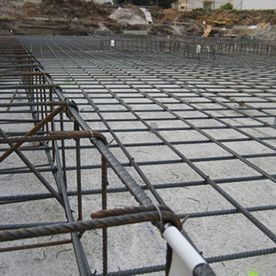 Rejilla de barras de acero colocada sobre una base de hormigón en una obra de construcción.