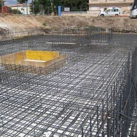Obra en construcción con cimentación de rejilla de barras de acero y un encofrado de hormigón amarillo en el centro.