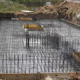 Malla de barras de refuerzo para una cimentación de hormigón en una obra de construcción, con un terraplén de tierra al fondo.