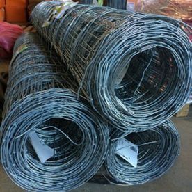 Bobinas de malla de alambre metálico laminado apiladas en el suelo de un almacén o taller.