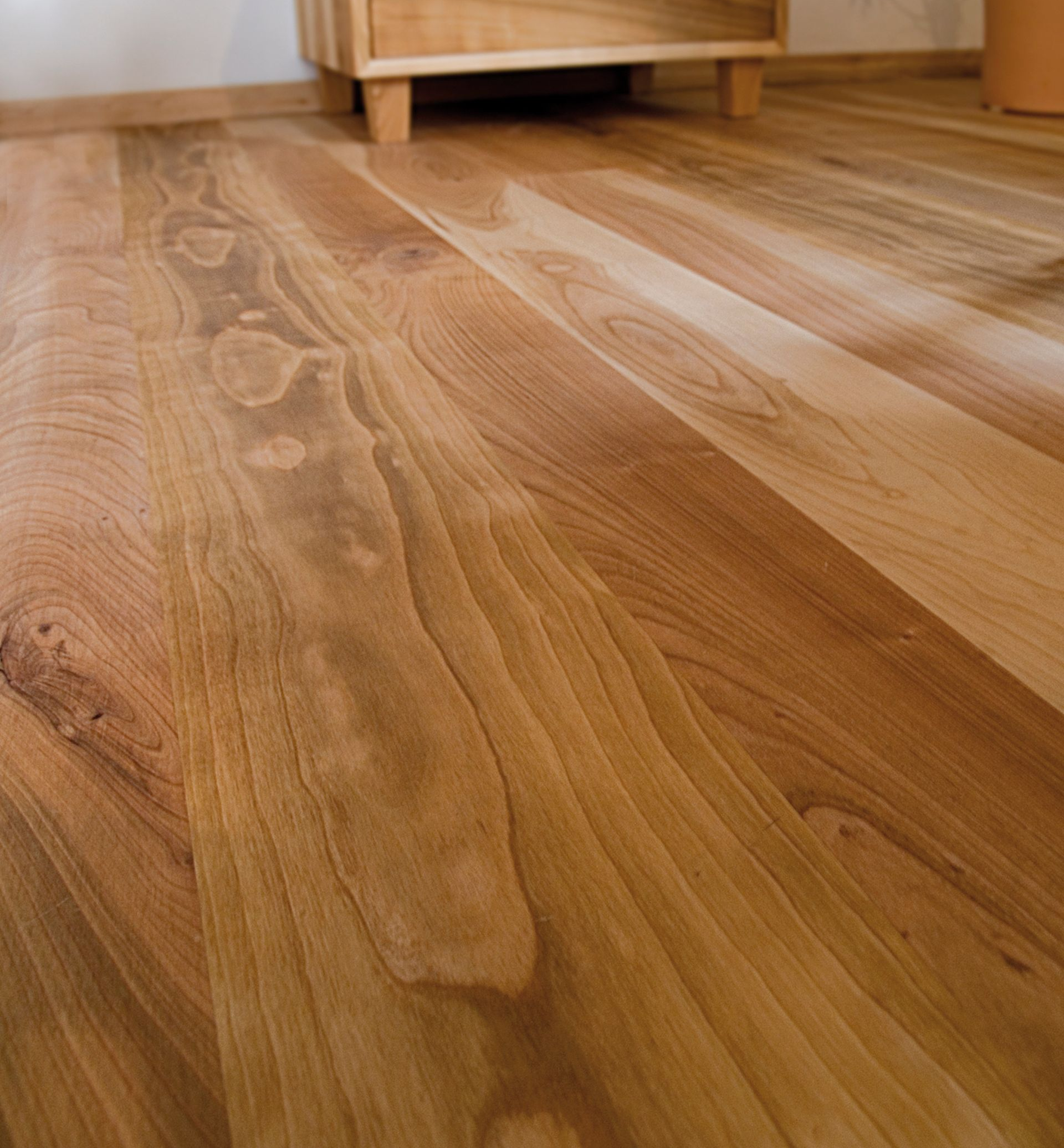 Parquet aux tons chauds et brun clair, reflétant la lumière naturelle. Meuble bas en arrière-plan.